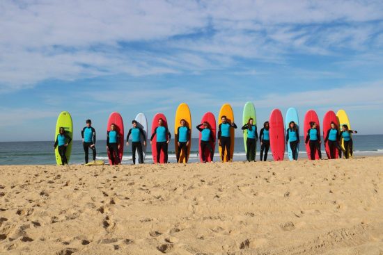 Groupe d'une douzaine de personnes en tenue de surf se tenant devant leurs planches, ces dernières étant plantées à la vertical dans le sable